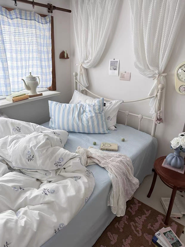 Bedroom with a bed featuring white bedding and striped pillows, curtains, and a clock.