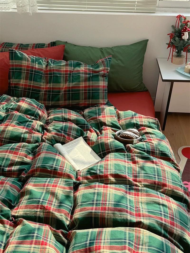 Plaid blanket and pillows on a bed with a side table and decorative items in the background.
