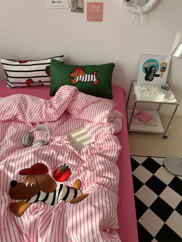 Bed with pink and white striped bedding featuring cartoon characters, next to a small table with decorative items.