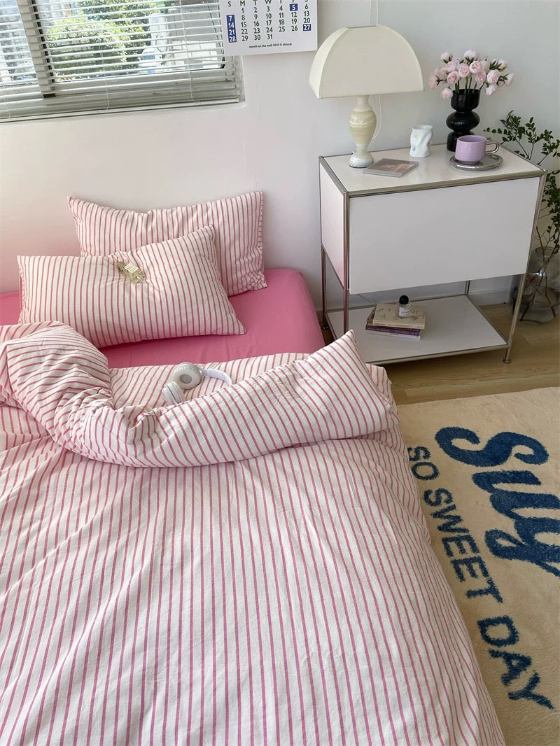 Bedroom with pink striped bedding and a nightstand with a lamp.