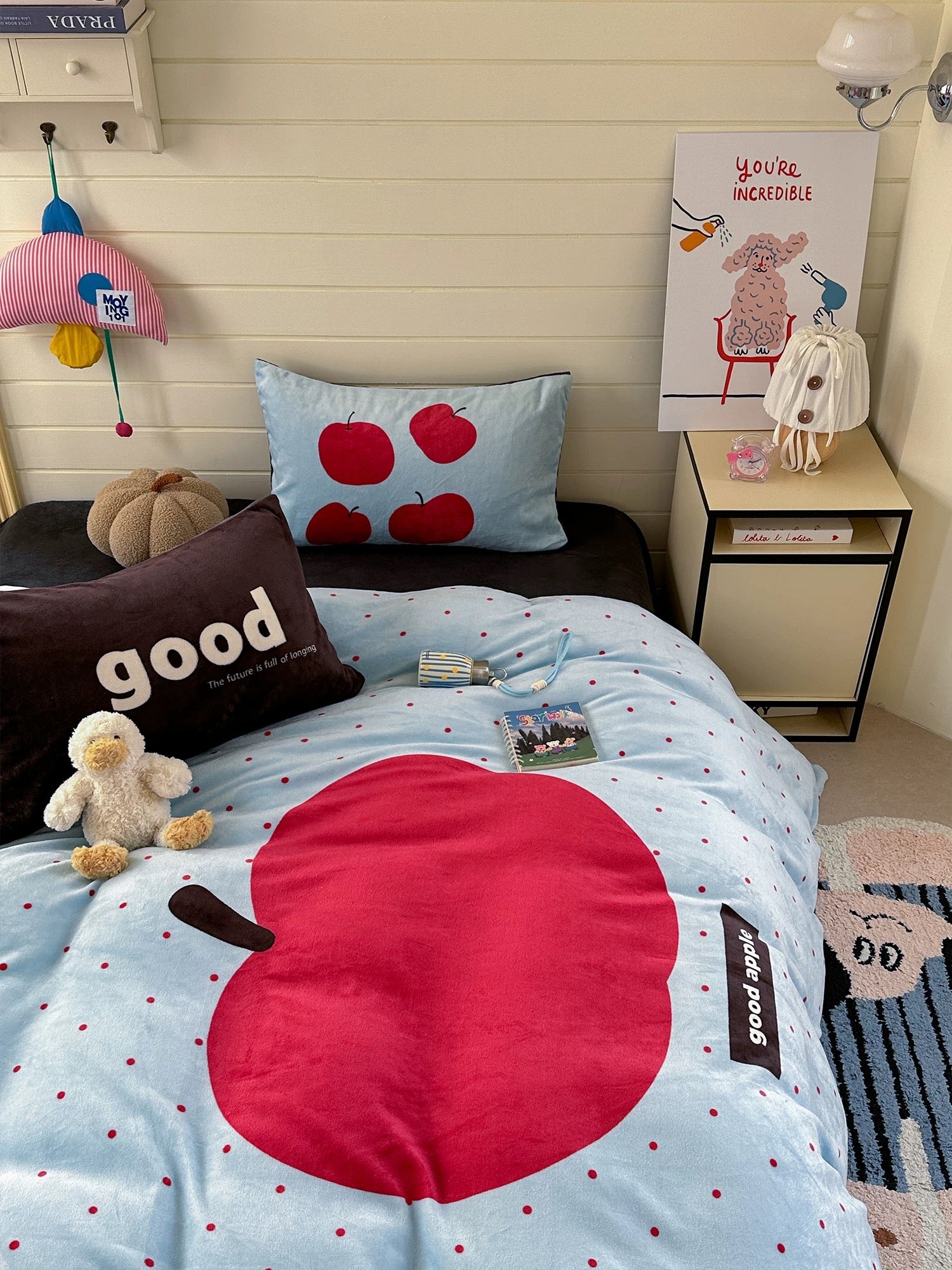 Children's bedroom with a bed featuring red apple designs, pillows, and a teddy bear.