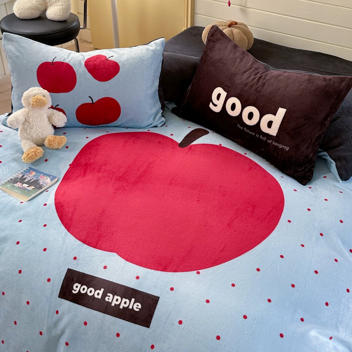 Bedspread with red apple design and 'good apple' text on a bed with decorative pillows.