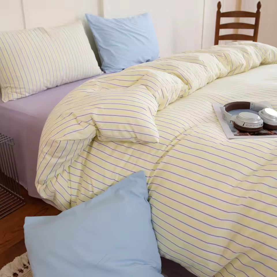 Bed with yellow and purple striped bedding and blue pillows.