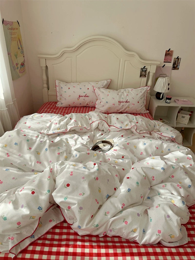 Bed with white floral bedding and red checkered blanket in a bedroom setting.