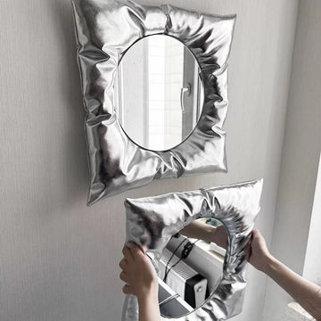 Silver inflatable mirror held by a person against a neutral background
