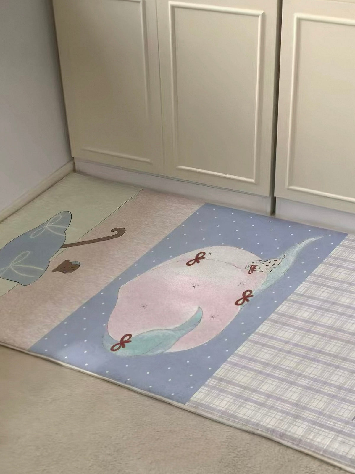 A cute runner rug with a pink peach and lilac checks sits flat in front of pale cabinet doors.