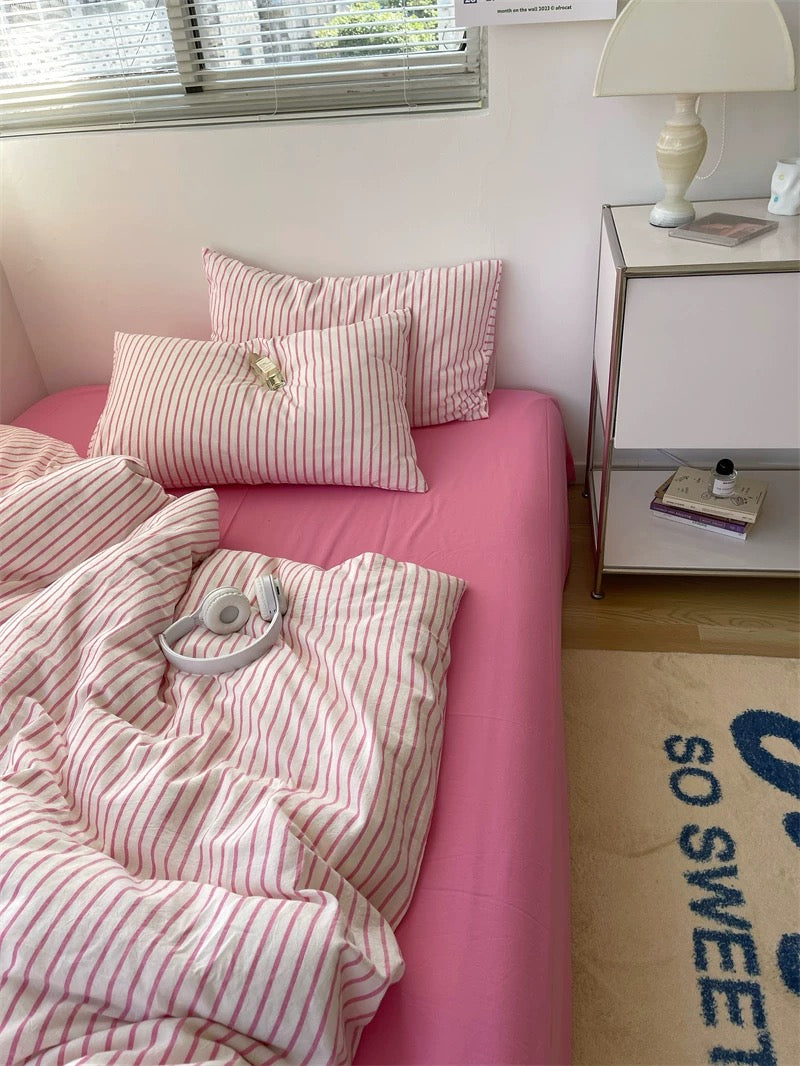 Bed with pink and white striped bedding and pillows, next to a nightstand with a lamp.