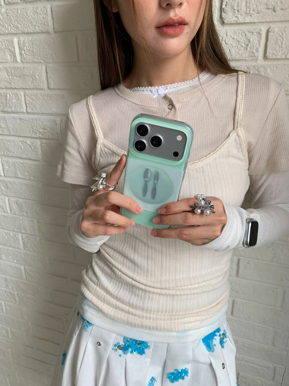 A matte phone case in mint green, held upright with a plate, spoon and fork design across the back.