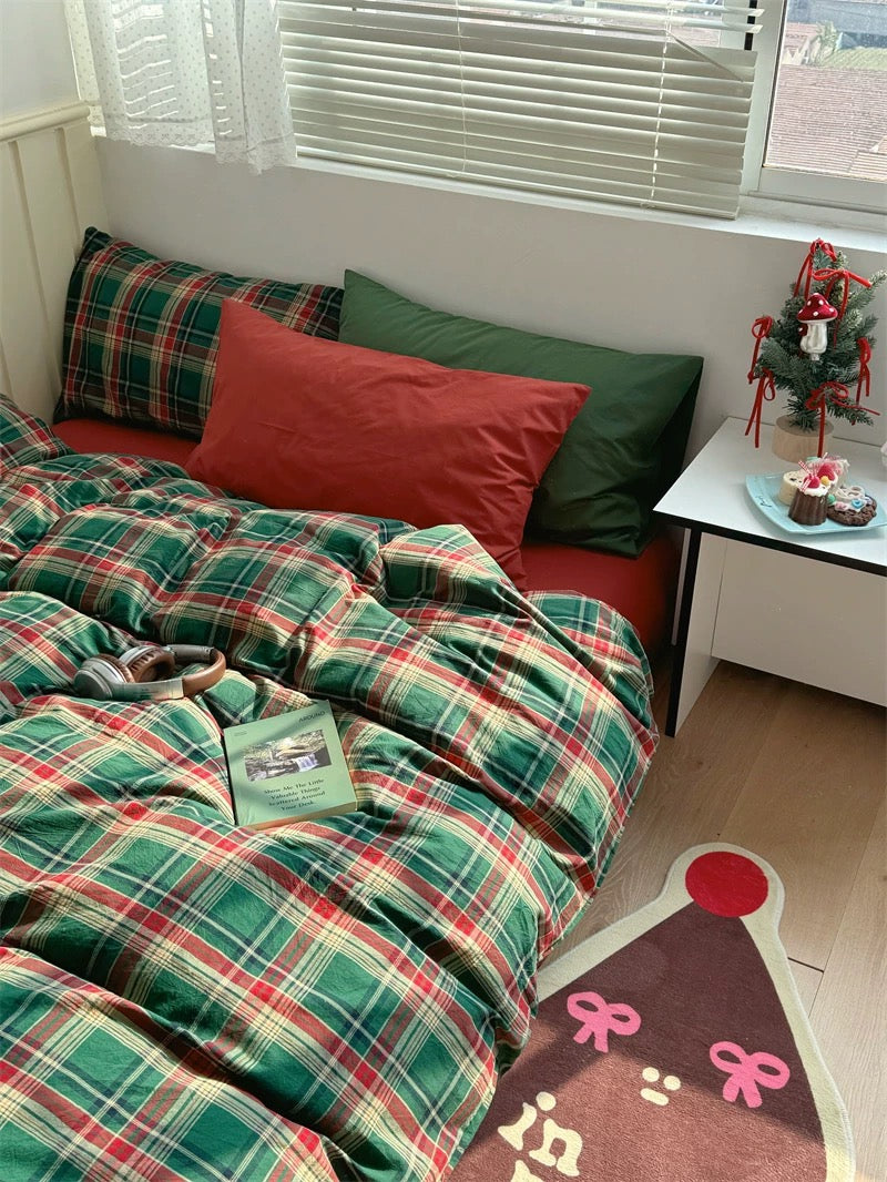 Bed with green and red plaid bedding in a room with a small table and decorative items.