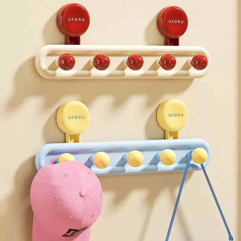 Two wall-mounted hook racks shown on a beige wall, one in red and one in yellow, each with multiple round hooks. A pink cap and blue strap hang from the lower rack.