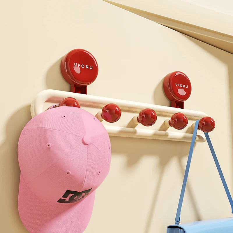 Blue wall hook rack with yellow ball hooks holding pink cap and small blue handbag.