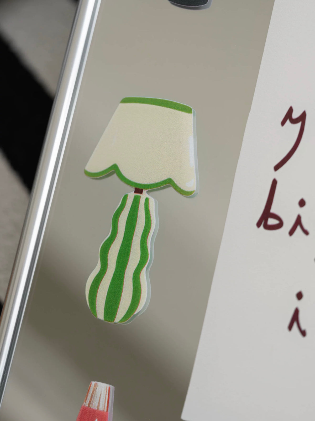 A decorative wall mirror close up shows a cream and green lamp illustration beside handwritten burgundy lettering.