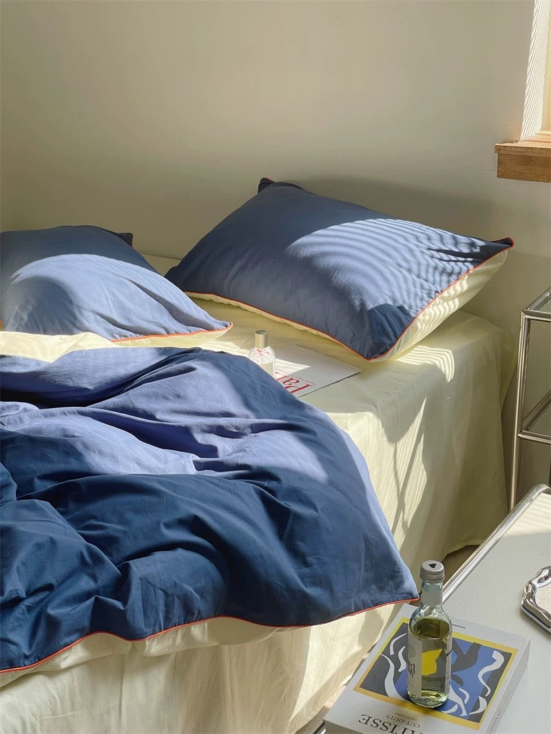 Blue bedding on a bed with a side table and bottle in the foreground
