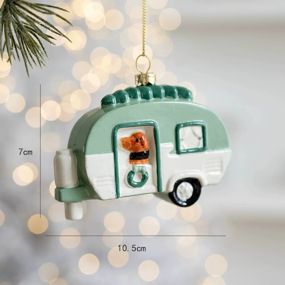 A dog camper ornament has a brown dog at the door, a green and white body and a small wreath.