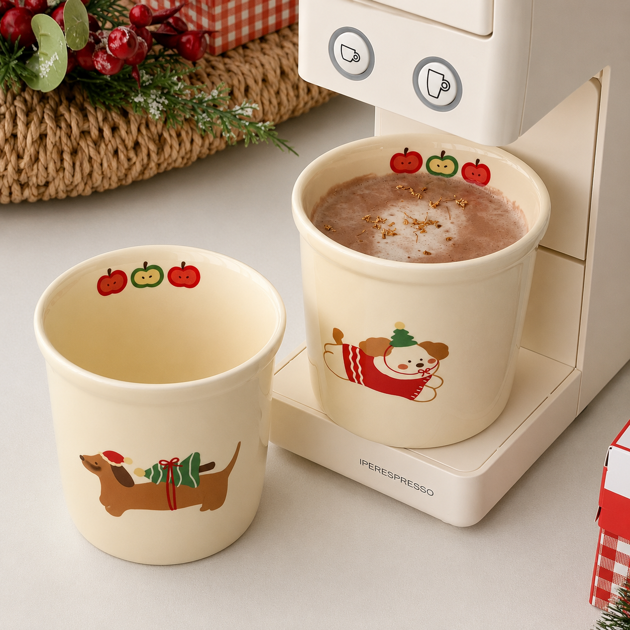 Two cream-colored ceramic mugs with Christmas-themed illustrations, one featuring a dachshund in a Santa hat and the other a snowman, shown next to a white coffee machine. One mug is empty, and the other is filled with a hot chocolate drink.