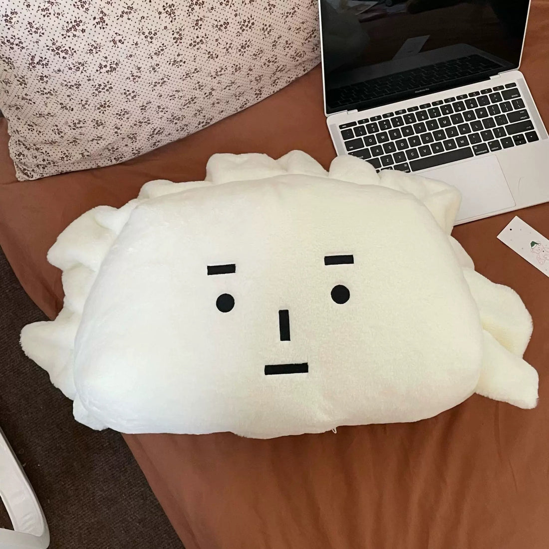 Plush toy resembling a cloud with a face on a desk next to a laptop