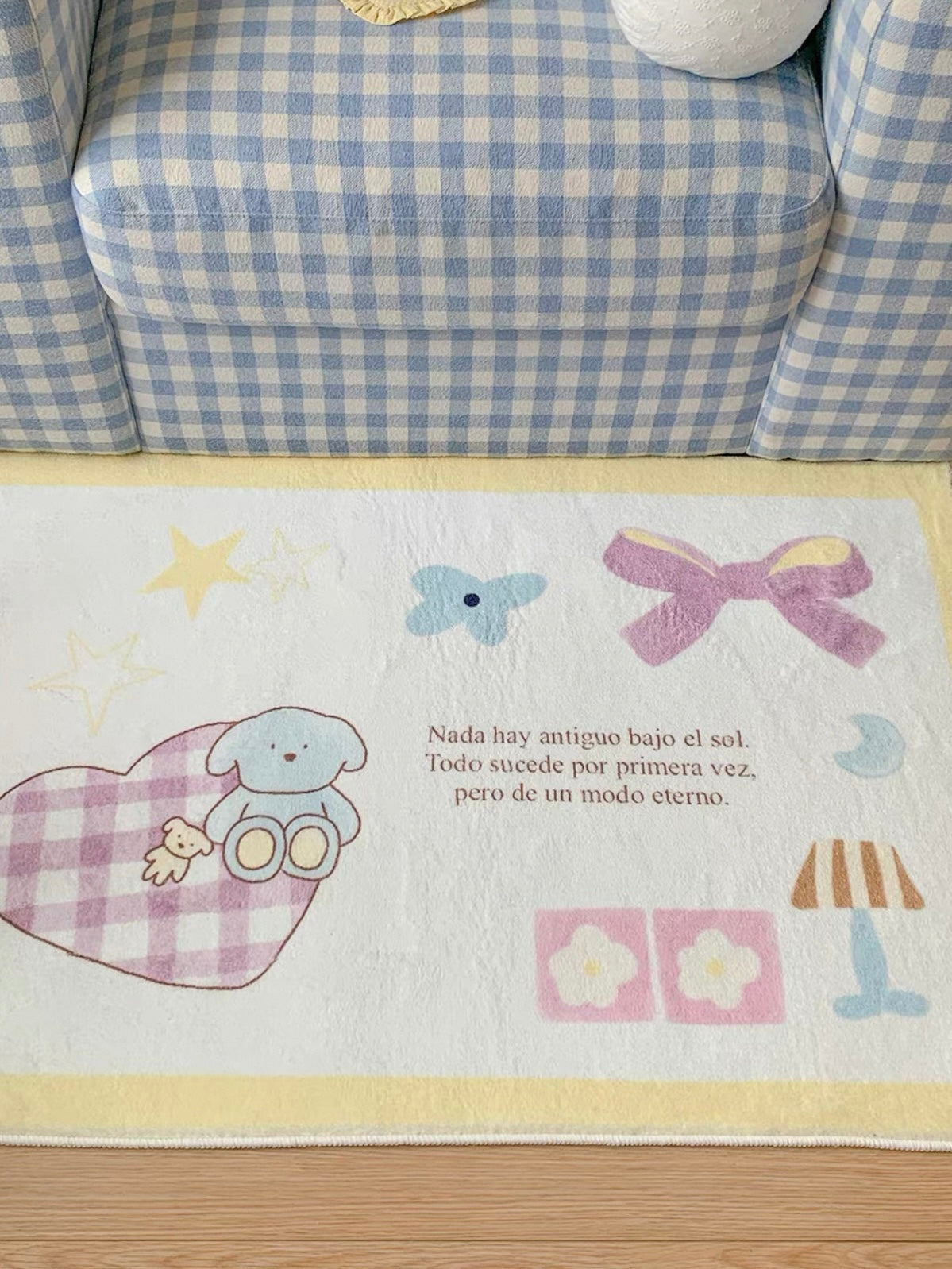 An elephant print rug with a yellow border shows a blue elephant on a checked heart, with a pink bow above.