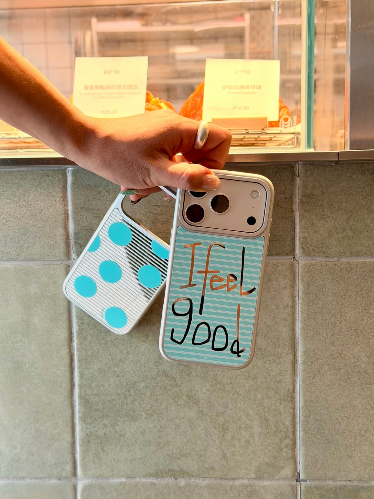 The Feel Good iPhone case hangs beside the aqua polka dot design, showing both patterned backs.