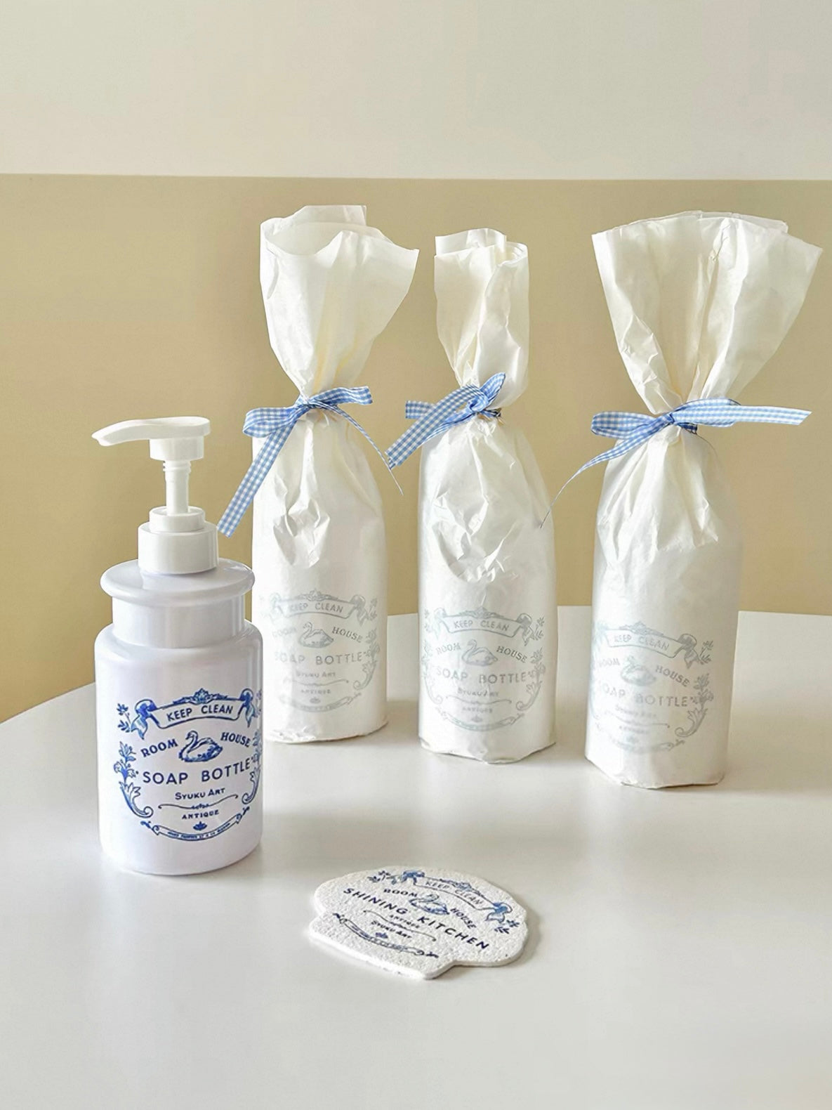 A floral soap dispenser stands beside wrapped bottles, with a matching blue and white sponge in front.
