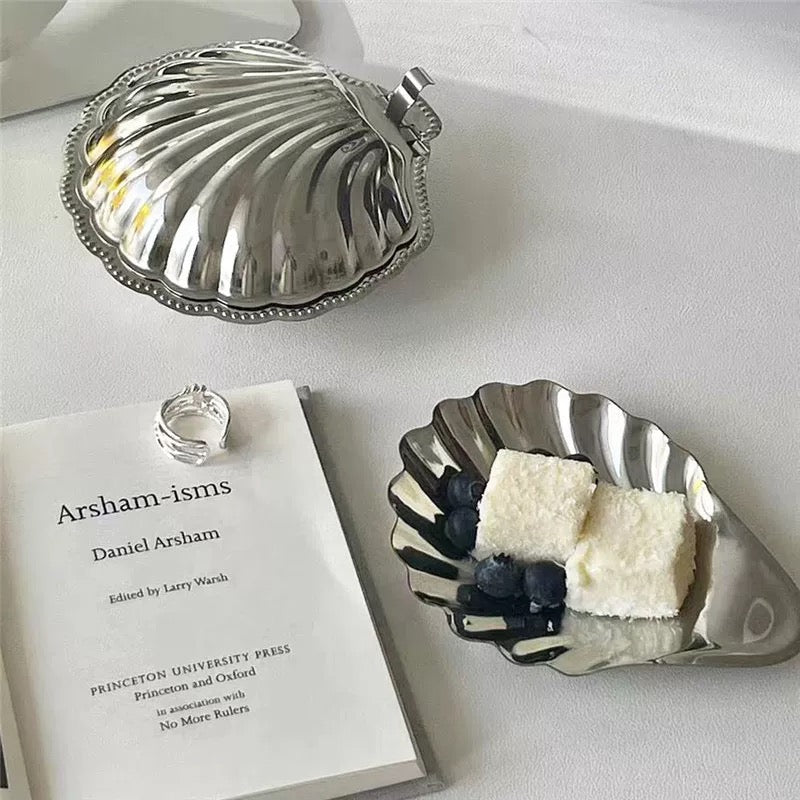 Silver shell-shaped dish with a book and dessert on a white surface
