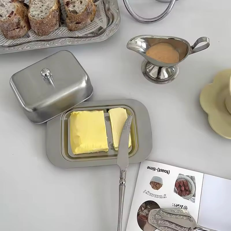 Butter dish with two pieces of butter, a knife, and a magazine on a white surface.