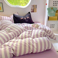 Side view of the bed dressed in purple striped bedding, complemented by pastel wall art