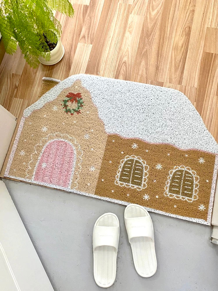 Cream gingerbread house doormat styled on wood flooring with white slippers