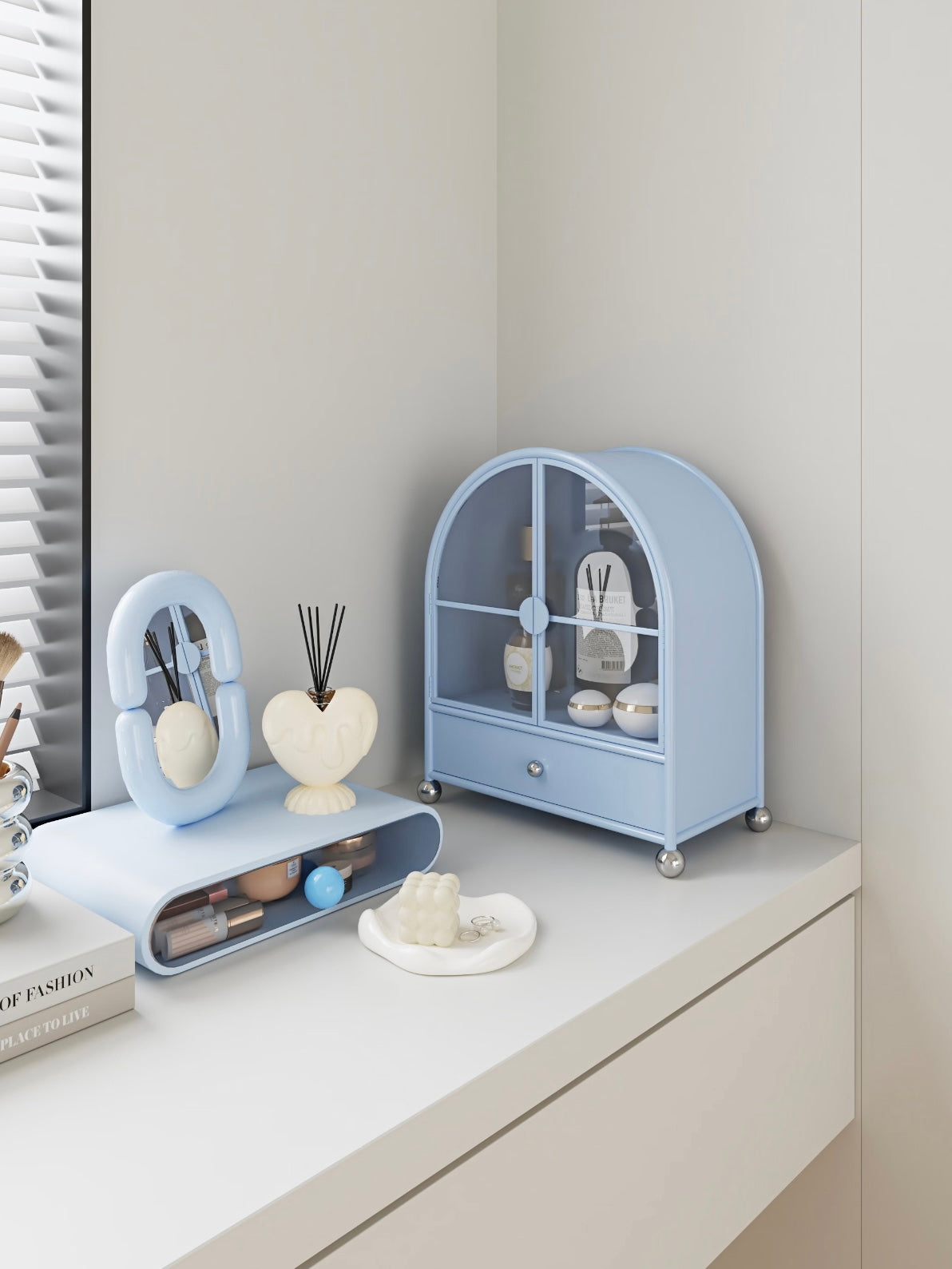 A blue glass makeup organizer stands at an angle on a dresser, with skincare bottles behind its doors.