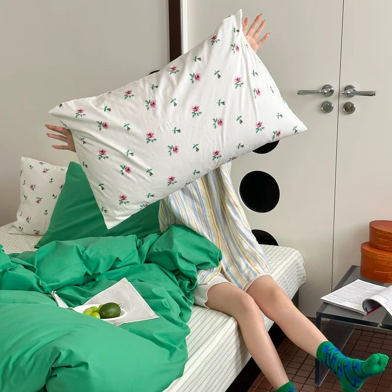 Person sitting on a bed with floral pillows and green bedding, holding a pillow above their head.
