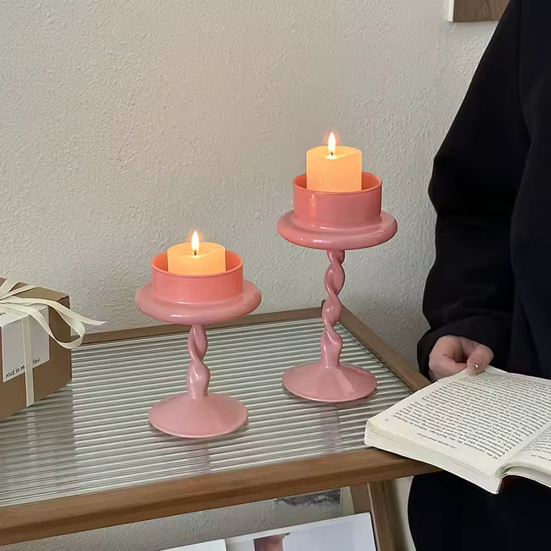 Two pink candle holders with candles on a table next to a person reading a book.