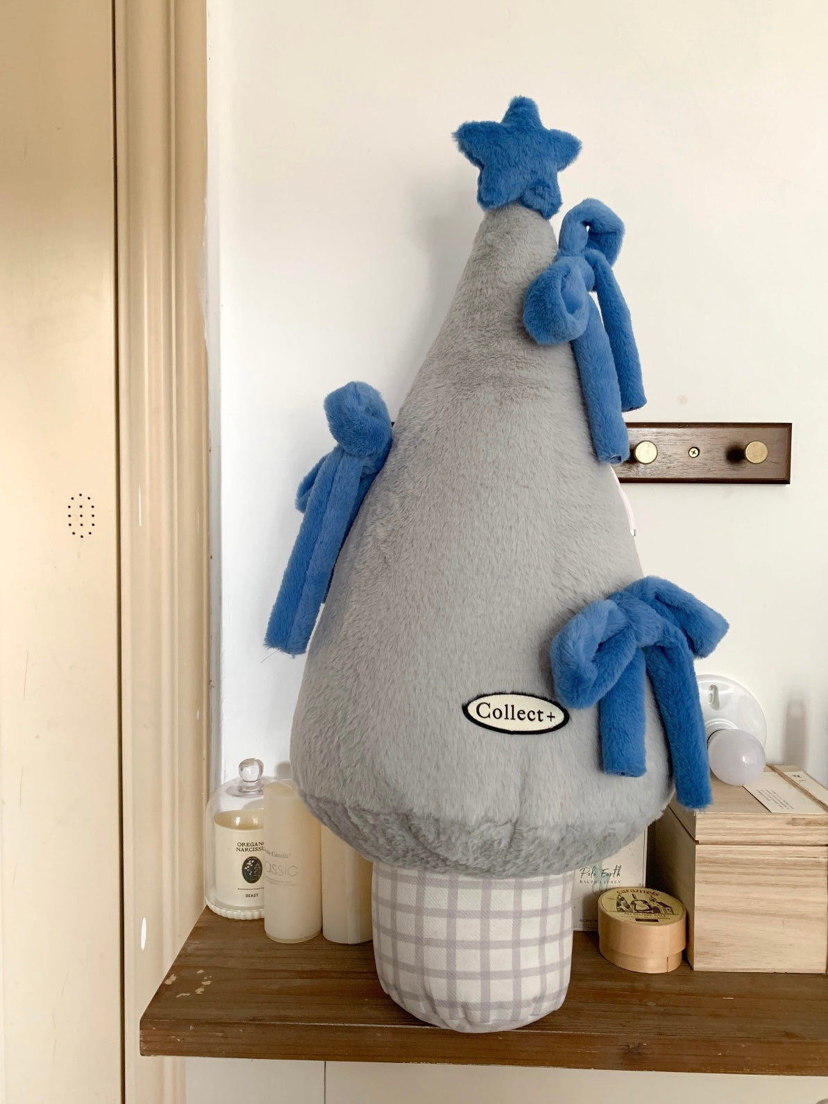 Gray plush Christmas tree pillow with blue bows displayed on a shelf