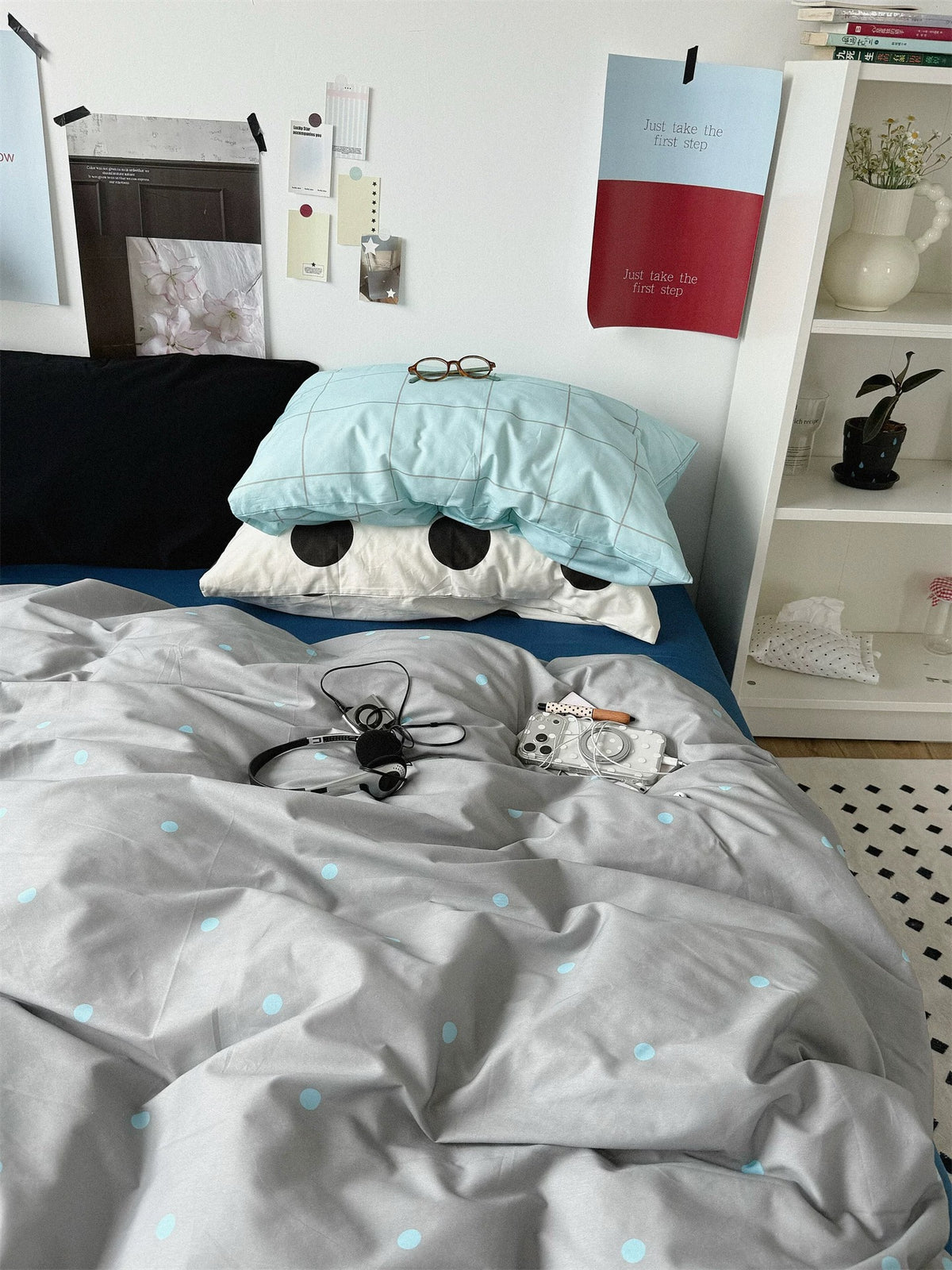 Gray polka dot duvet cover with a black pillow and stacked blue check and black dot cases.