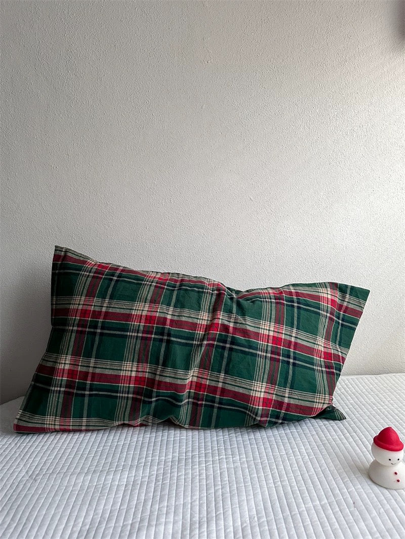 A green and red tartan pillowcase shows overlapping checks and thin cream lines.