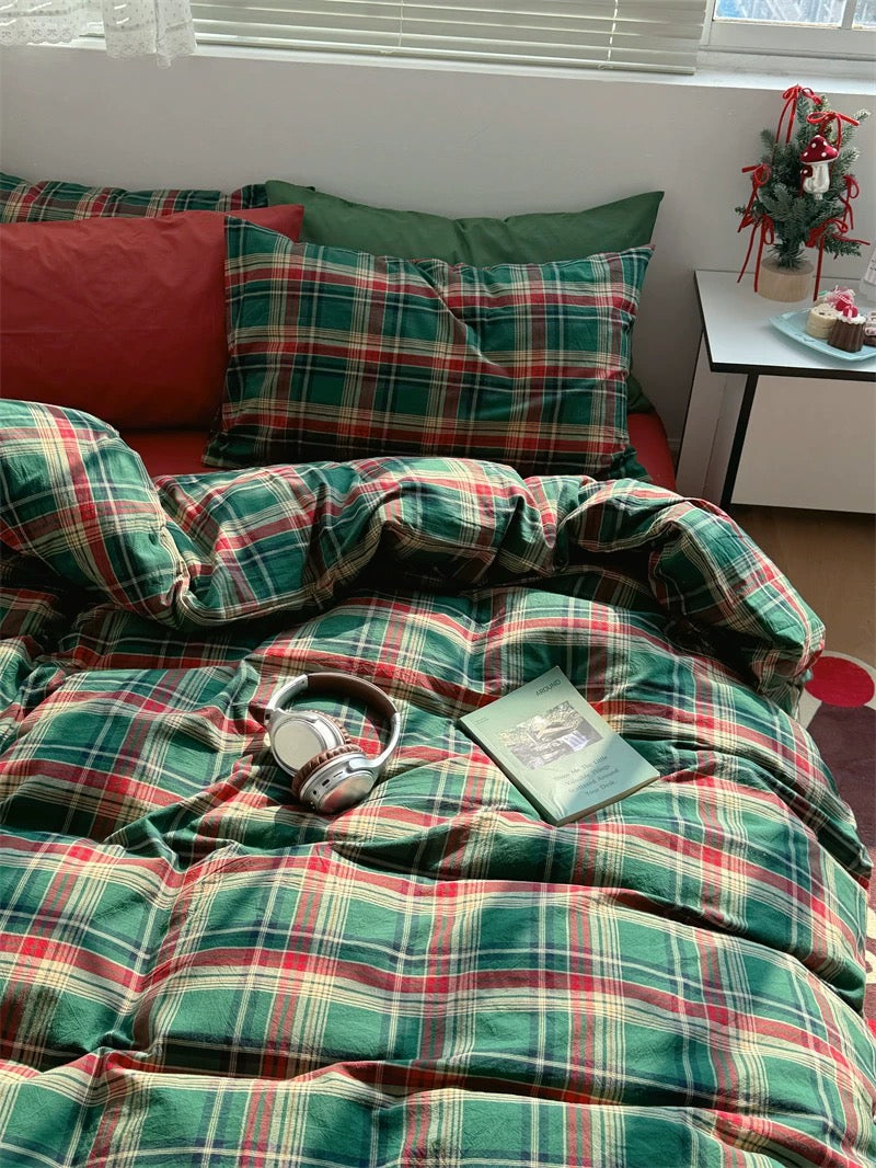 Plaid bedspread on a bed with pillows and a small table in the corner.