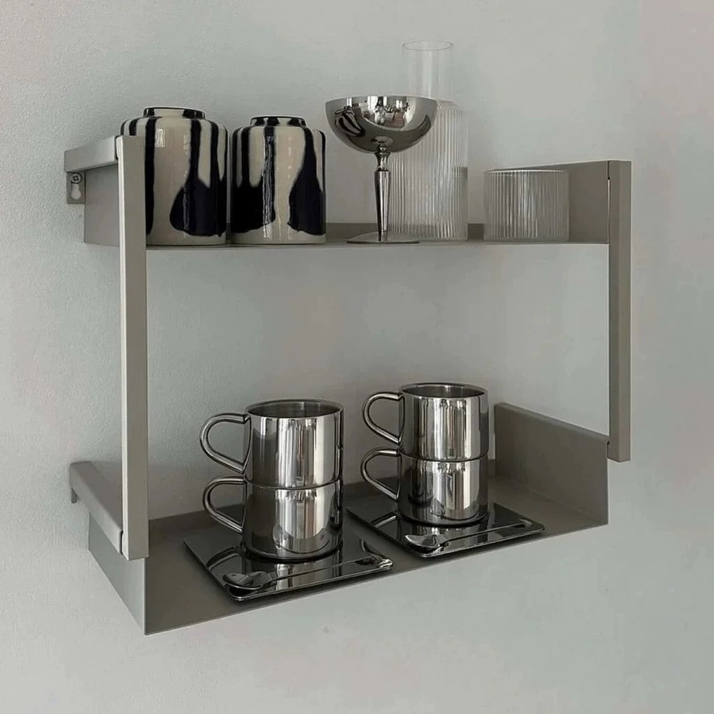 Metallic coffee mugs on a shelf with decorative items against a light gray background