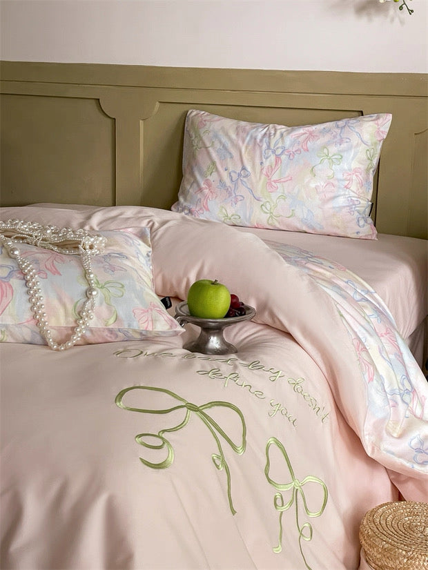 Bed with embroidered pink bedding and floral pillowcases, featuring an apple on a stand.