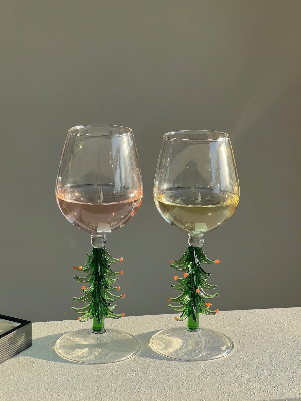 Holiday wine glasses with green Christmas tree stems beside stacked books