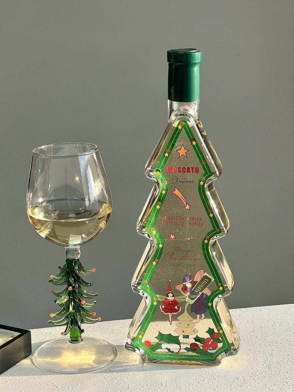 Christmas tree wine glasses beside a decorative holiday tree on a tabletop