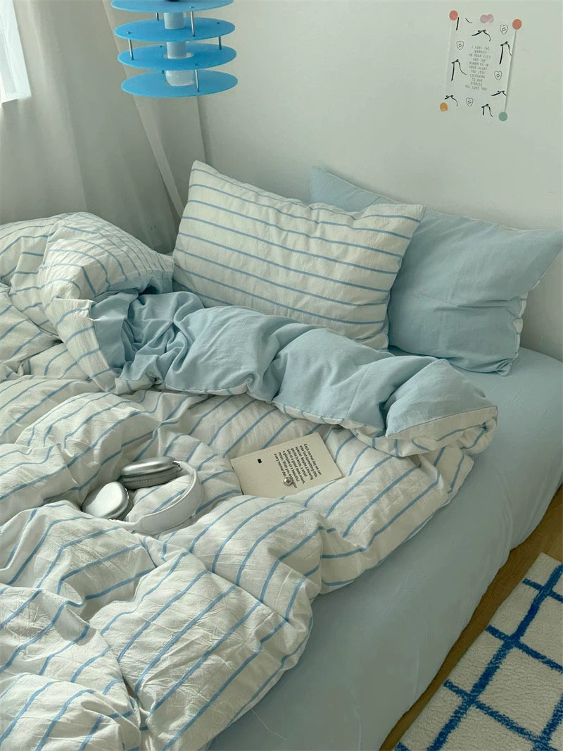 Bed with light blue and white striped bedding in a room with a blue hanging lamp and wall decorations.