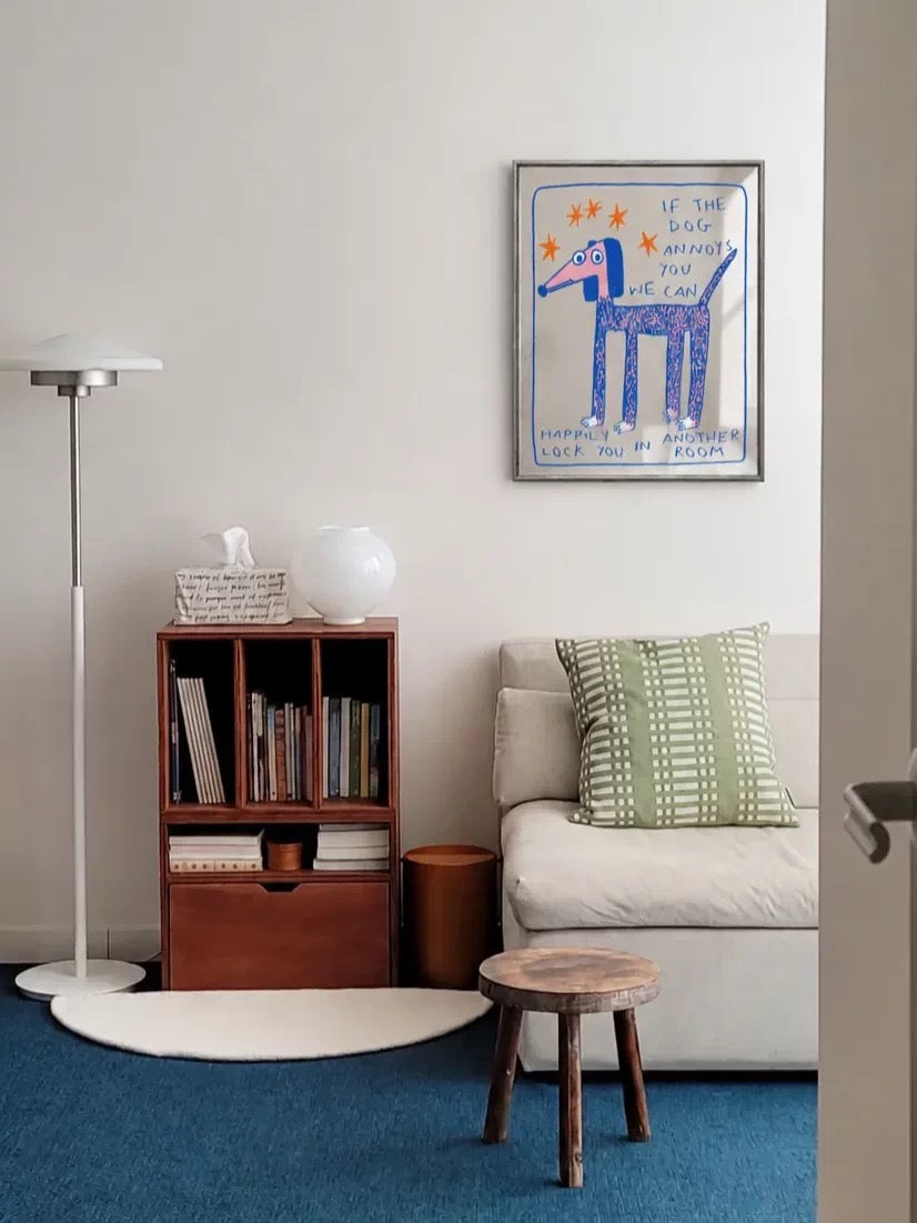 An illustrated dog wall mirror hangs above a chair, with blue lettering and orange stars inside a silver frame.