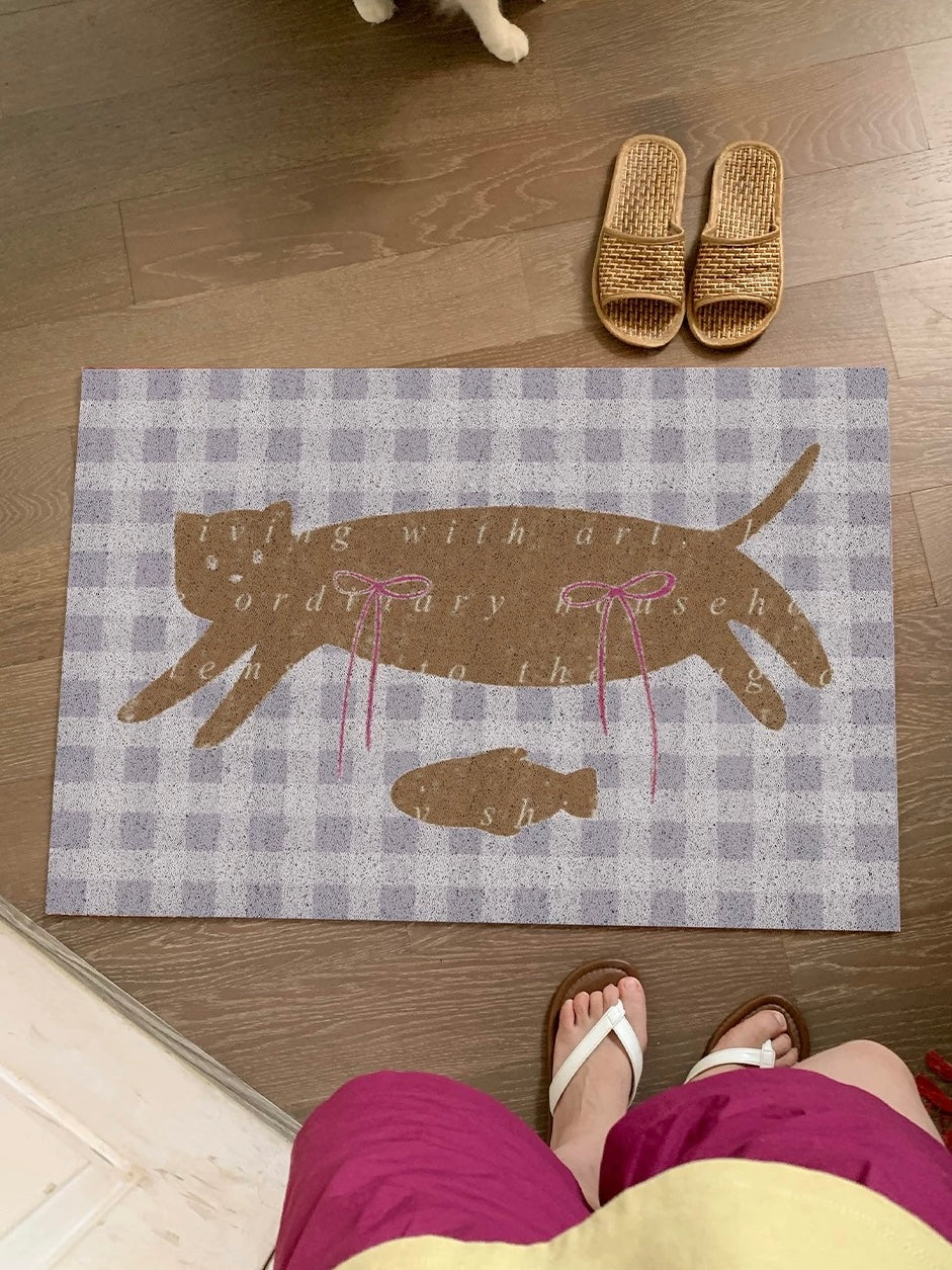 An indoor door mat with a brown cat and pink bows sits across a doorway on a purple and white gingham base.