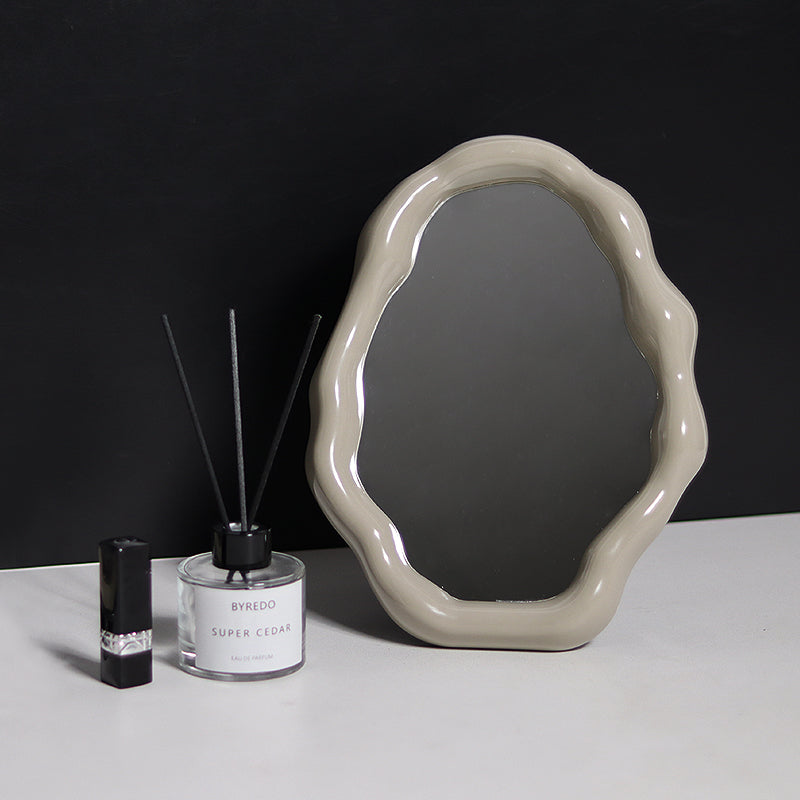 Decorative mirror with a black tray holding a bottle, small box, and other items on a light surface.