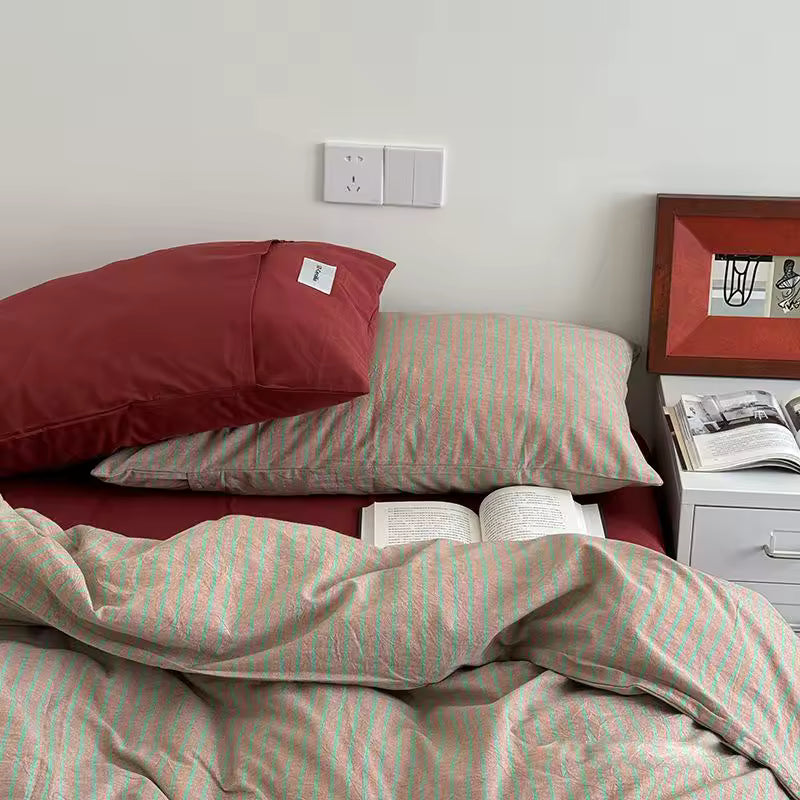 Bed with striped bedding and pillows, nightstand with books in the corner
