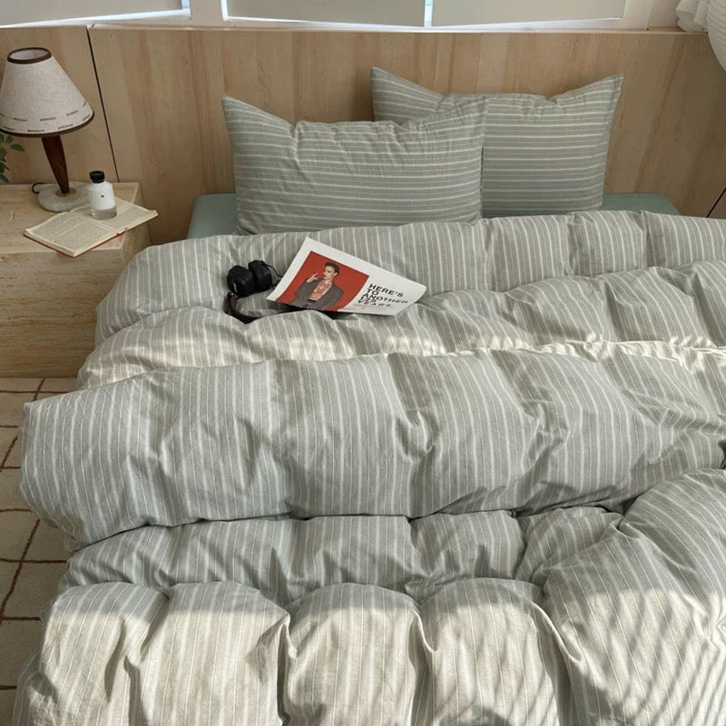 Bed with striped bedding and pillows, featuring a magazine and a small dog on a wooden floor.