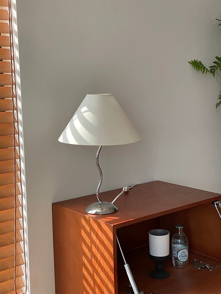 White lamp on a wooden shelf with a plant in the corner