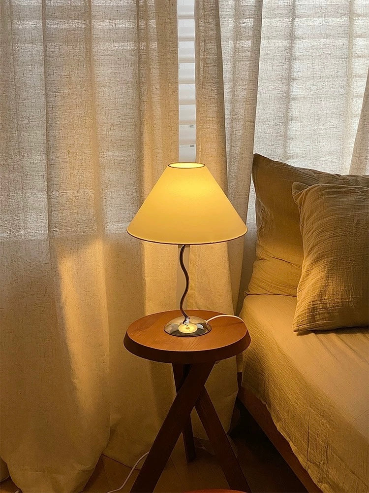 Lamp on a small round table next to a bed with curtains in the background
