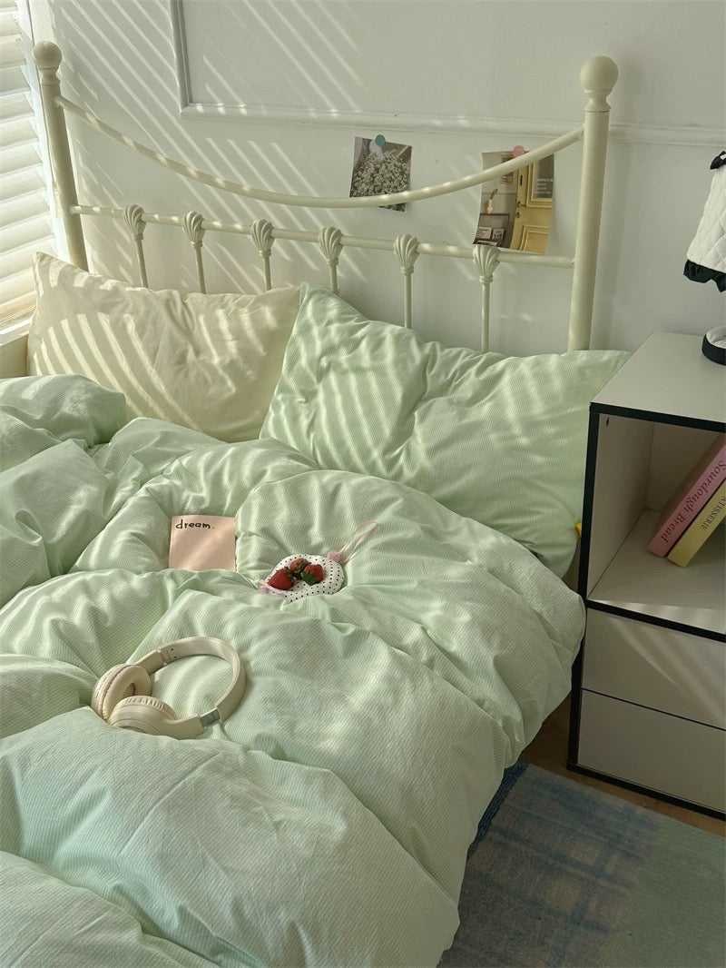 Light green comforter set on a bed with a white nightstand in a bedroom.