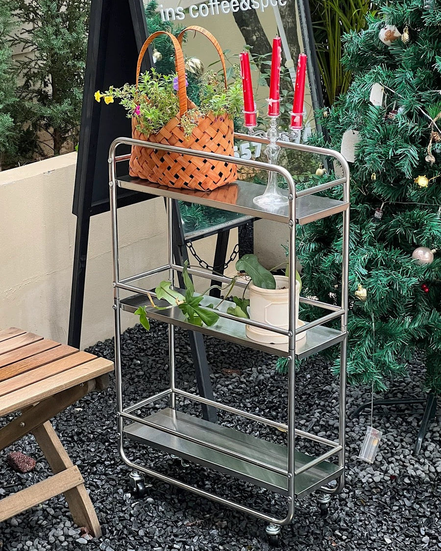 Three-tier chrome rolling cart with open shelves used for candles, mugs, and decorative storage.
