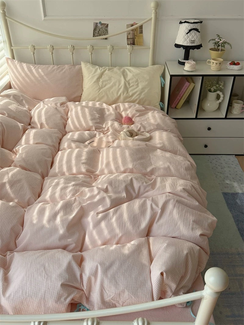 Pink textured comforter on a bed in a room with a shelf and decor items.