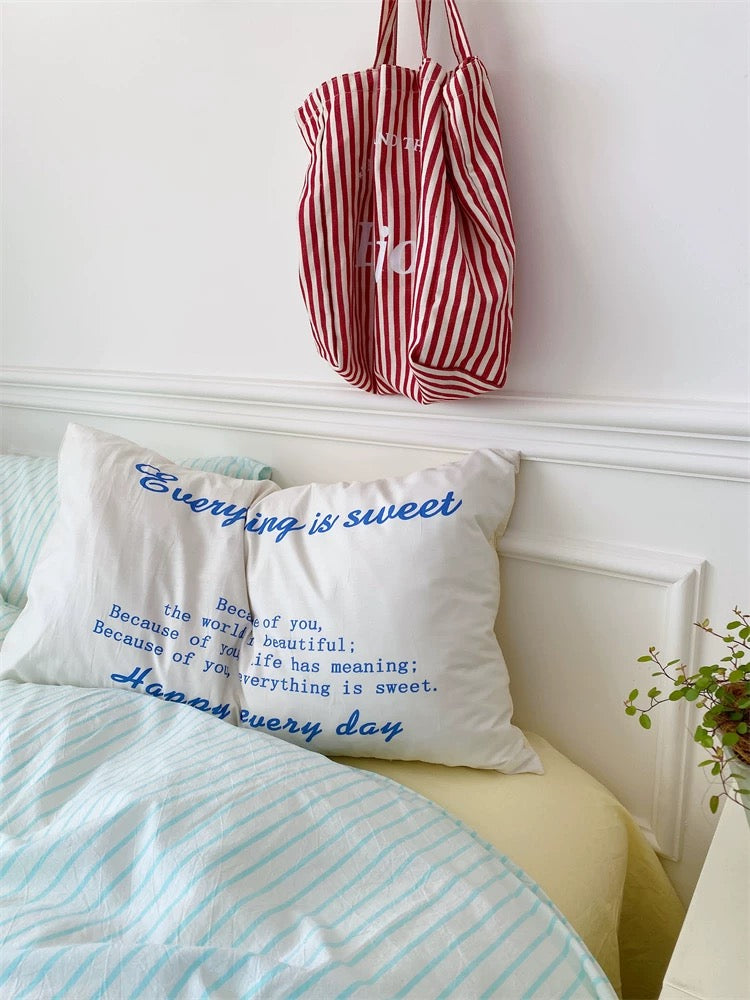 Striped bag hanging above a bed with pillows featuring text, against a white wall.